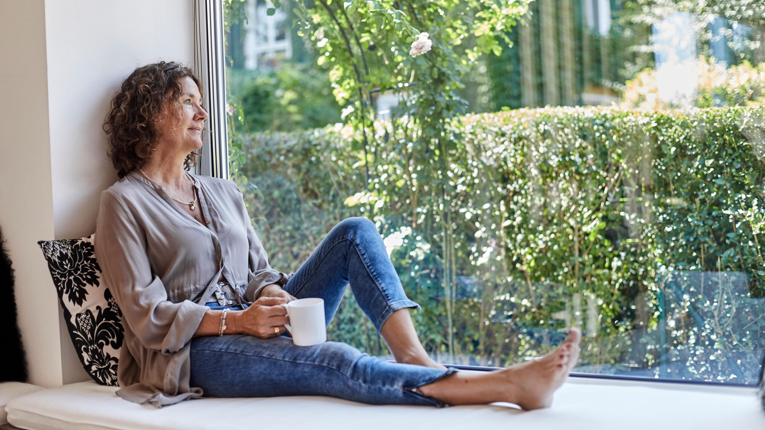 Woman relaxing by a sunny window with a mug.